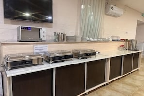 A buffet setup with a microwave, hot plates, and utensils.