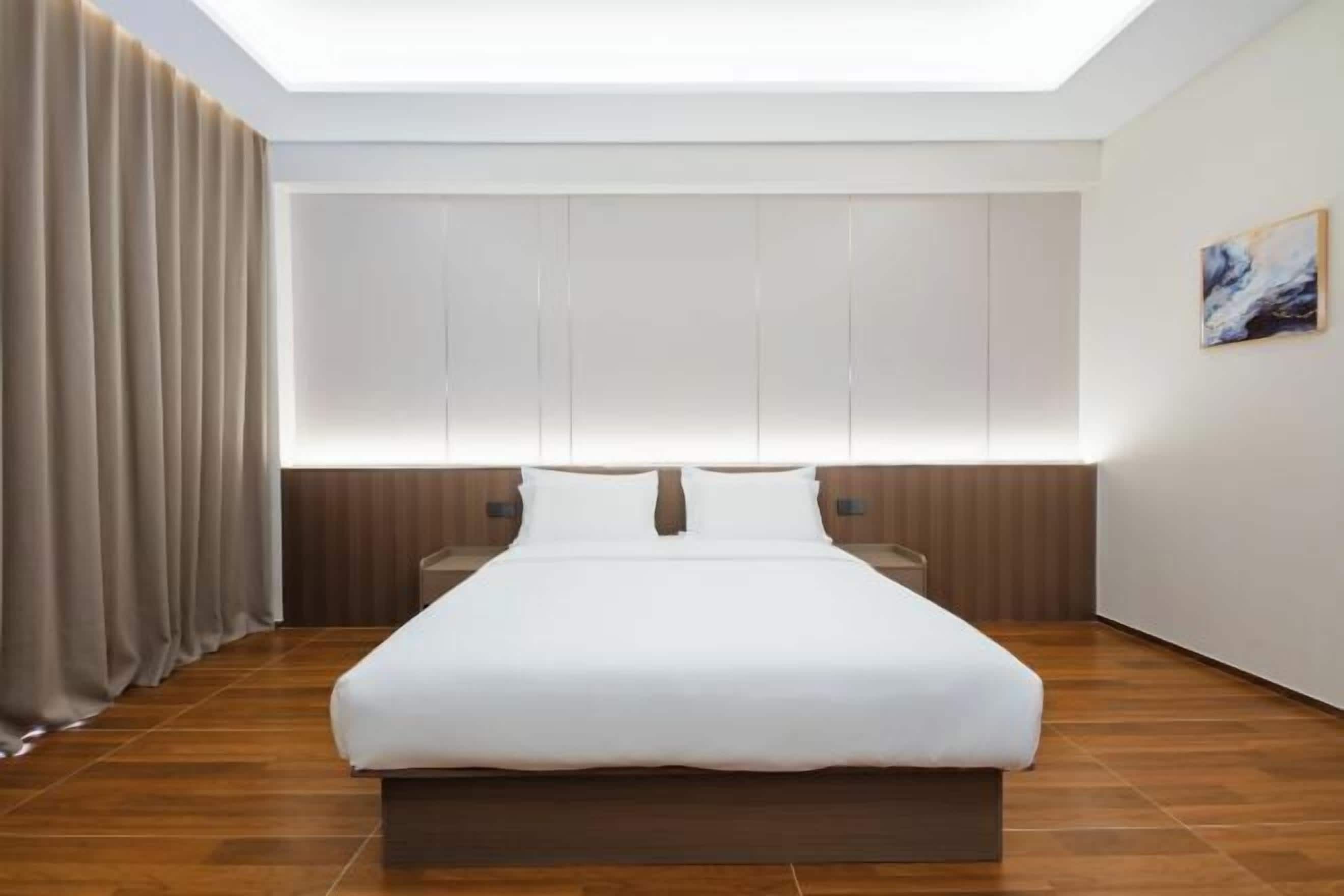 A modern hotel room with a large bed, wooden flooring, a skylight, and a painting on the wall.