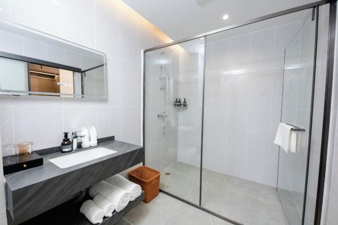 A modern bathroom with a glass-enclosed shower, a dark marble countertop, and a white sink.