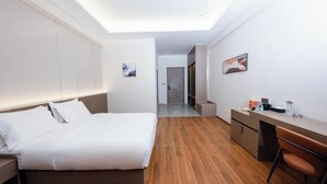 A modern hotel room with a bed, desk, and chair, a walk-in closet, and a hallway leading to another room. - New Junlong Hotel (Bavet)