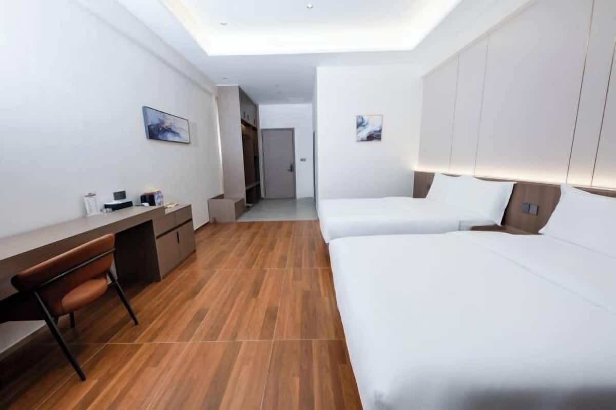 Une chambre d’hôtel moderne avec un plancher en bois, un bureau avec une chaise, deux lits et des œuvres d’art accrochées aux murs.