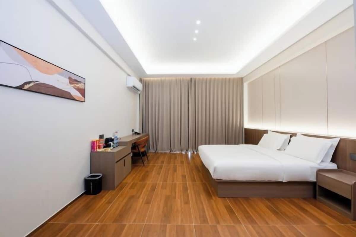 Une chambre d’hôtel moderne, équipée d’un lit, d’un bureau et d’une chaise, avec un tableau au mur et un luminaire au plafond.