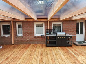 A covered patio with a wooden deck, a grill, and brick walls. - Active country home near the Baltic Sea with a pool and orchard, perfect for family and friends (Lübow)
