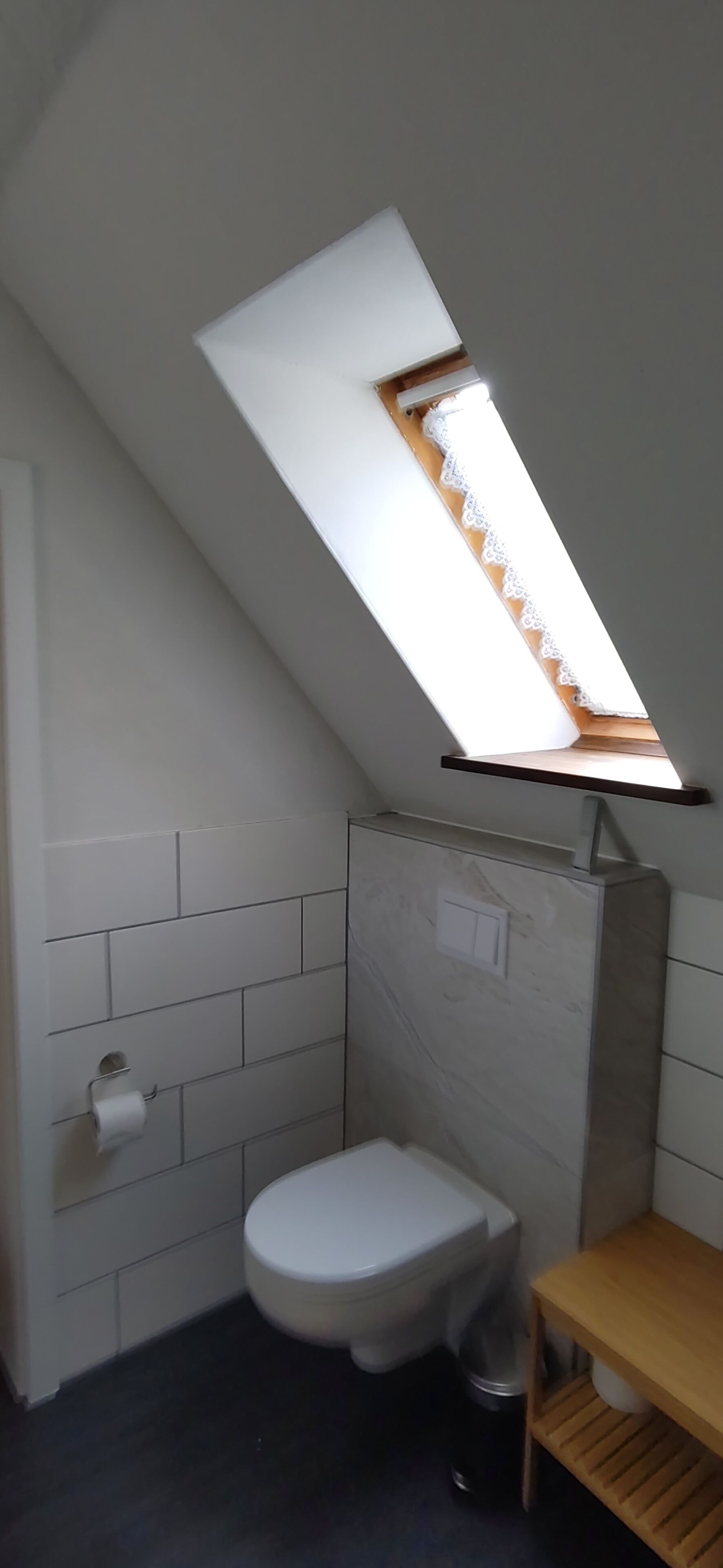Ein kleines Badezimmer mit Oberlicht, Toilette und Holzregal.