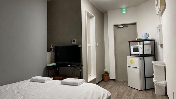 A hotel room with a bed, a desk with a TV, a microwave, and a trash bin. - Tokyo guest (Tokyo)