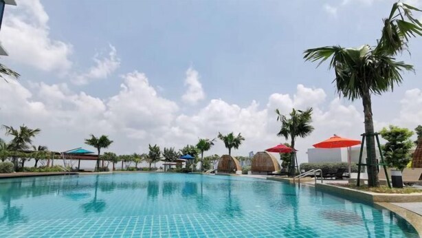 A swimming pool with tiled edges, surrounded by palm trees and umbrellas. - C2011 Almas Suites Studio Netflix Johor by STAY (Iskandar Puteri)
