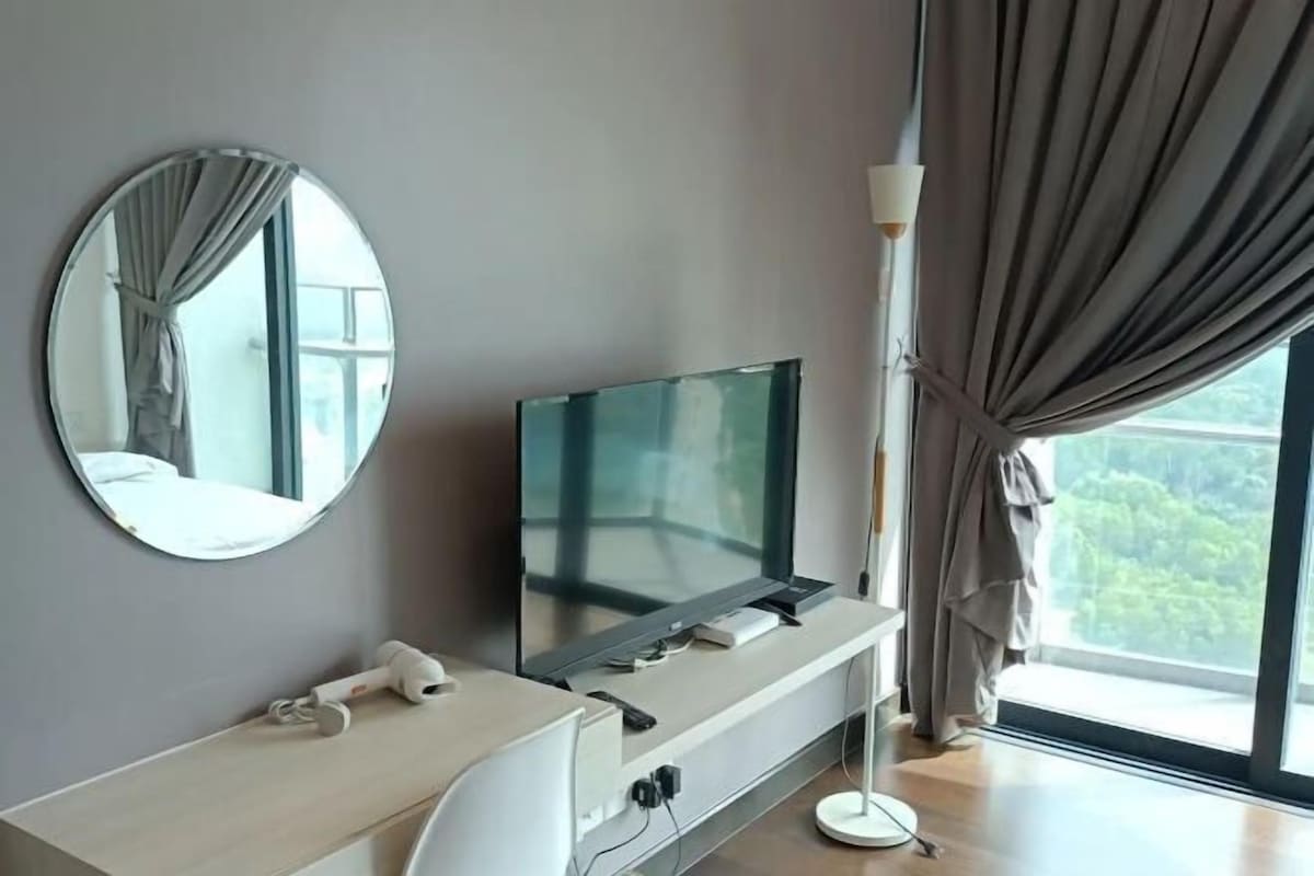 Una camera d'albergo moderna con televisione a schermo piatto su una consolle bianca, uno specchio rotondo a parete e un'ampia finestra con tende.