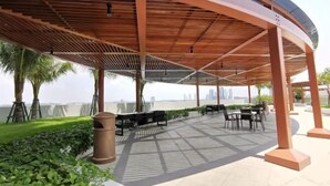 An outdoor patio with a curved wooden roof, seating areas, and a view of the city skyline. - C2011 Almas Suites Studio Netflix Johor by STAY (Iskandar Puteri)