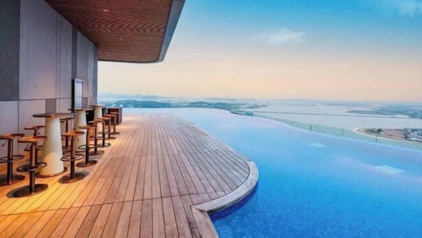 A rooftop infinity pool with wooden deck seating and a view of a river and distant landscape. - A La Carte Ha Long Apartments by Kevin & Anna (Ha Long)