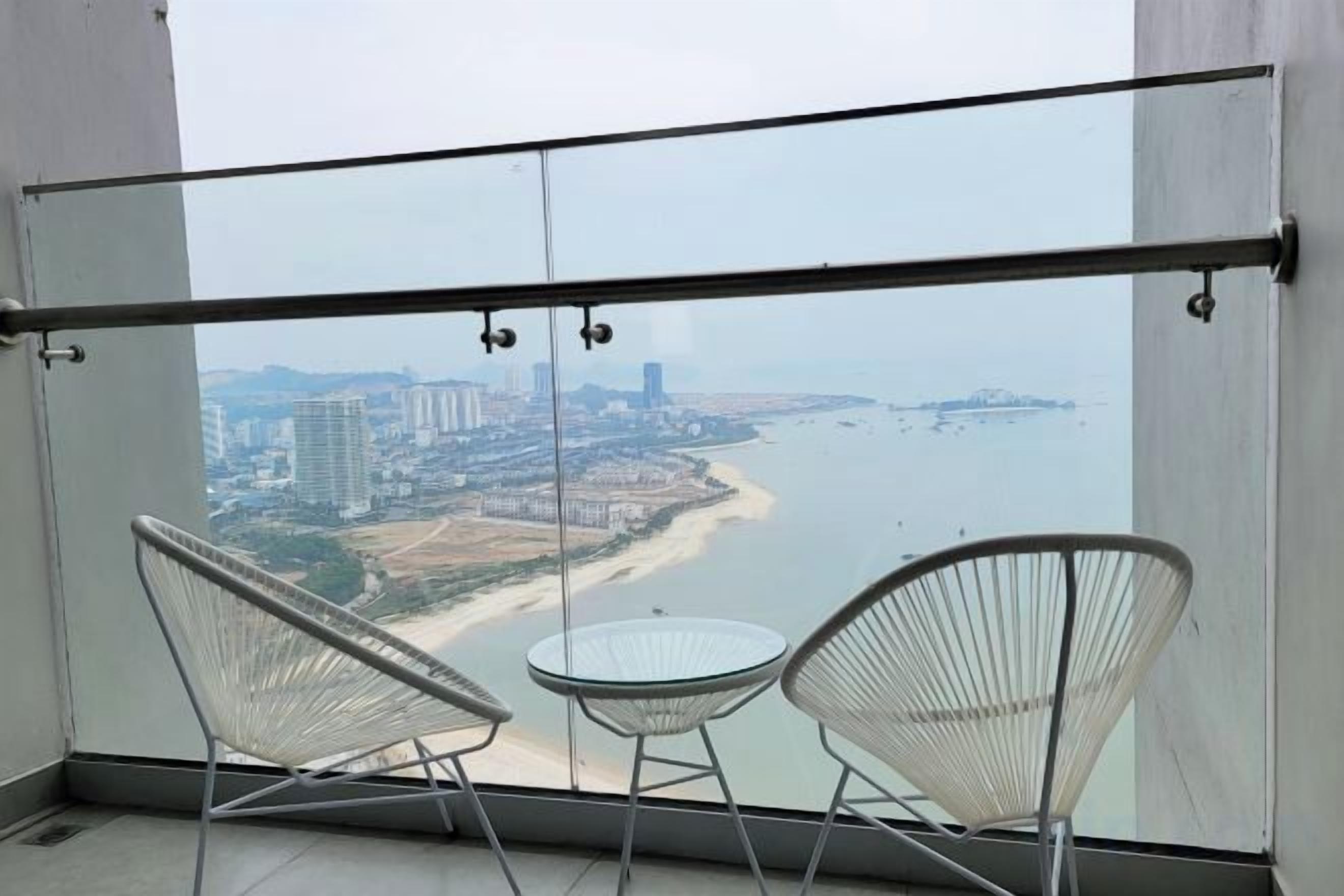 Ein Balkon mit zwei Stühlen und einem Tisch, mit Blick auf Strand und Stadtlandschaft.