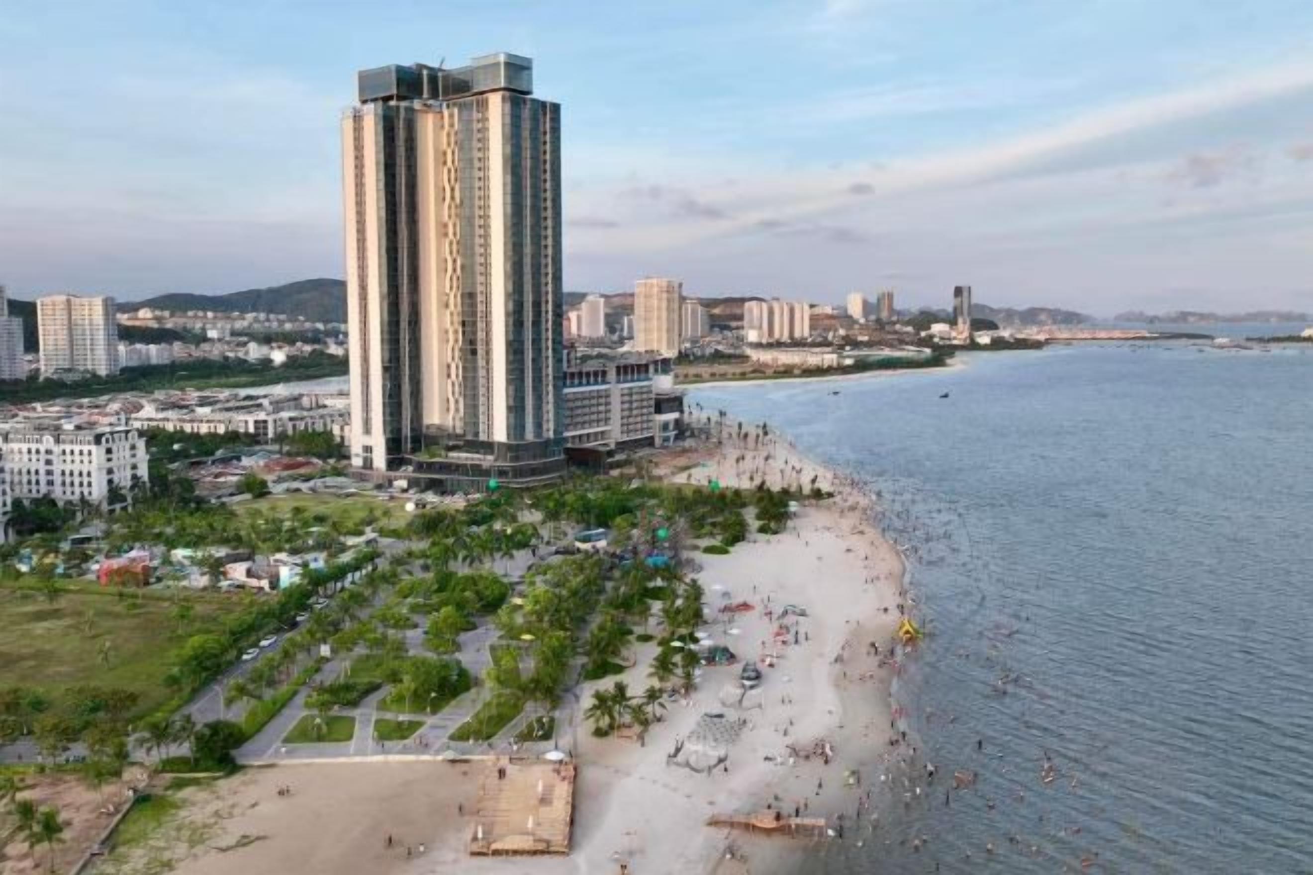 Un paysage urbain côtier avec un grand hôtel qui domine l’horizon, une plage et un port de plaisance.