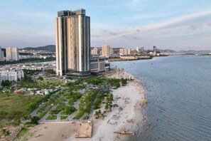 A coastal cityscape with a prominent high-rise hotel, a beach, and a marina. - A La Carte Ha Long Bay Apartments by Kevin & Anna (Ha Long)