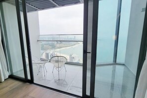 A balcony with a glass door, two chairs, and a view of a beach and cityscape. - A La Carte Ha Long Bay Apartments by Kevin & Anna (Ha Long)