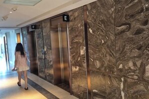 An interior corridor with marble walls and an elevator marked with letters E and F. - A La Carte Ha Long Bay Apartments by Kevin & Anna (Ha Long)