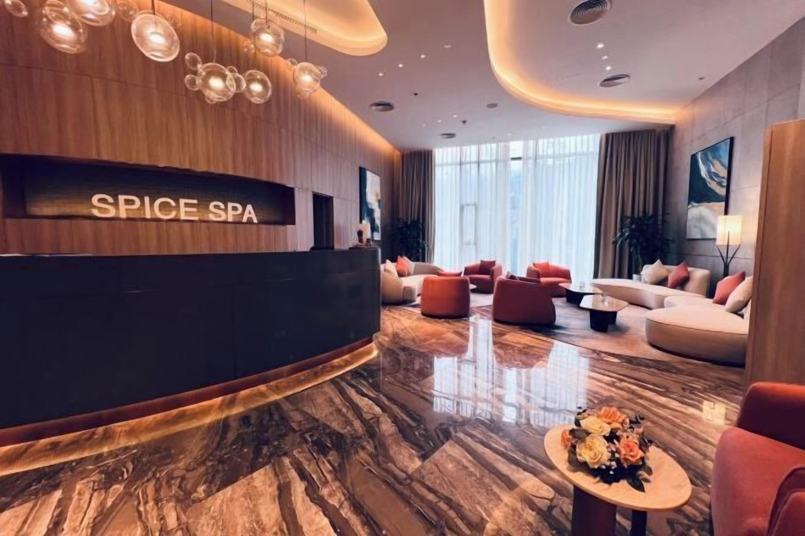 A modern spa lobby with a reception desk labeled "SPICE SPA," plush seating, and a marble floor.