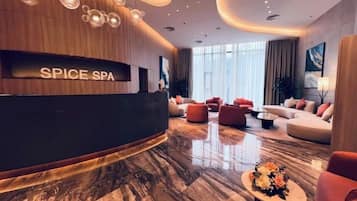 A modern spa lobby with a reception desk labeled "SPICE SPA," plush seating, and a marble floor.