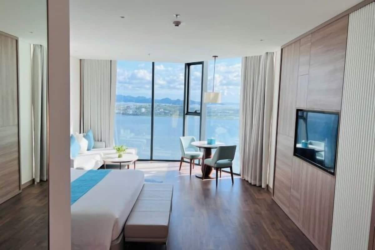 A modern hotel room with a large bed, a seating area with a table, and a TV mounted on the wall.