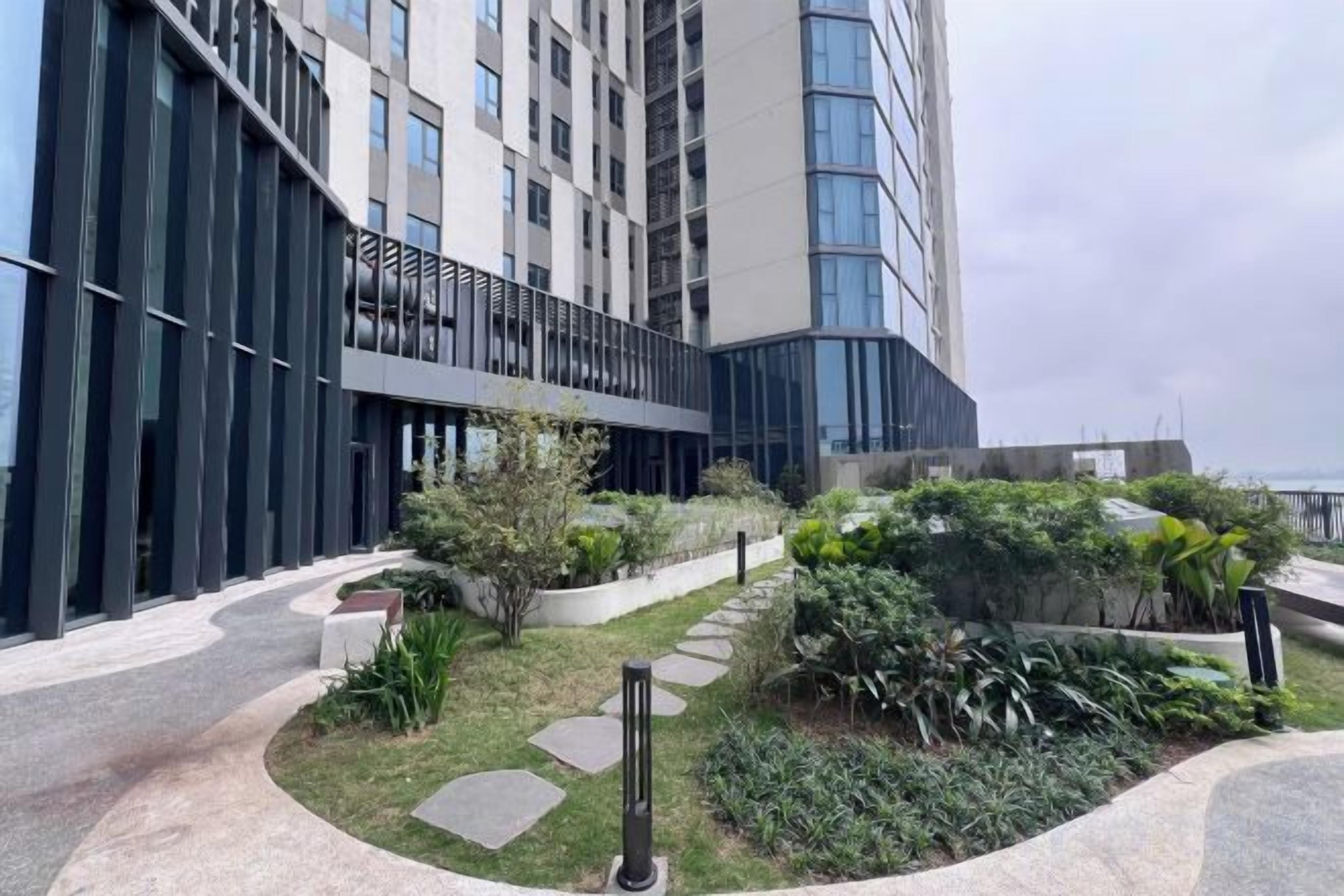 Ein modernes Gebäude mit Glasfassade, ein angelegter Gartenbereich mit Wegen und Blick aufs Meer.