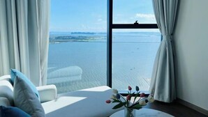 A room with a large window, a white sofa, and a vase with flowers. - A La Carte Ha Long Apartments by Kevin & Anna (Ha Long)
