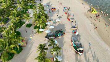 A beach with palm trees, umbrellas, and people.