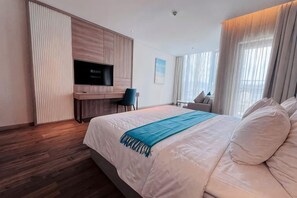 Une chambre d’hôtel moderne, dotée d’un grand lit, d’une télévision, d’un bureau et offrant une vue sur l’extérieur.