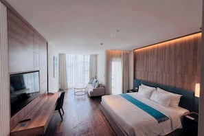 Ein modernes Hotelzimmer mit einem großen Bett, einem Schreibtisch mit Flachbildfernseher und einer Sitzecke mit einer Couch.