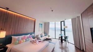 A modern hotel room with a large bed, a sofa, a small table, and a view of the city. - A La Carte Ha Long Apartments by Kevin & Anna (Ha Long)