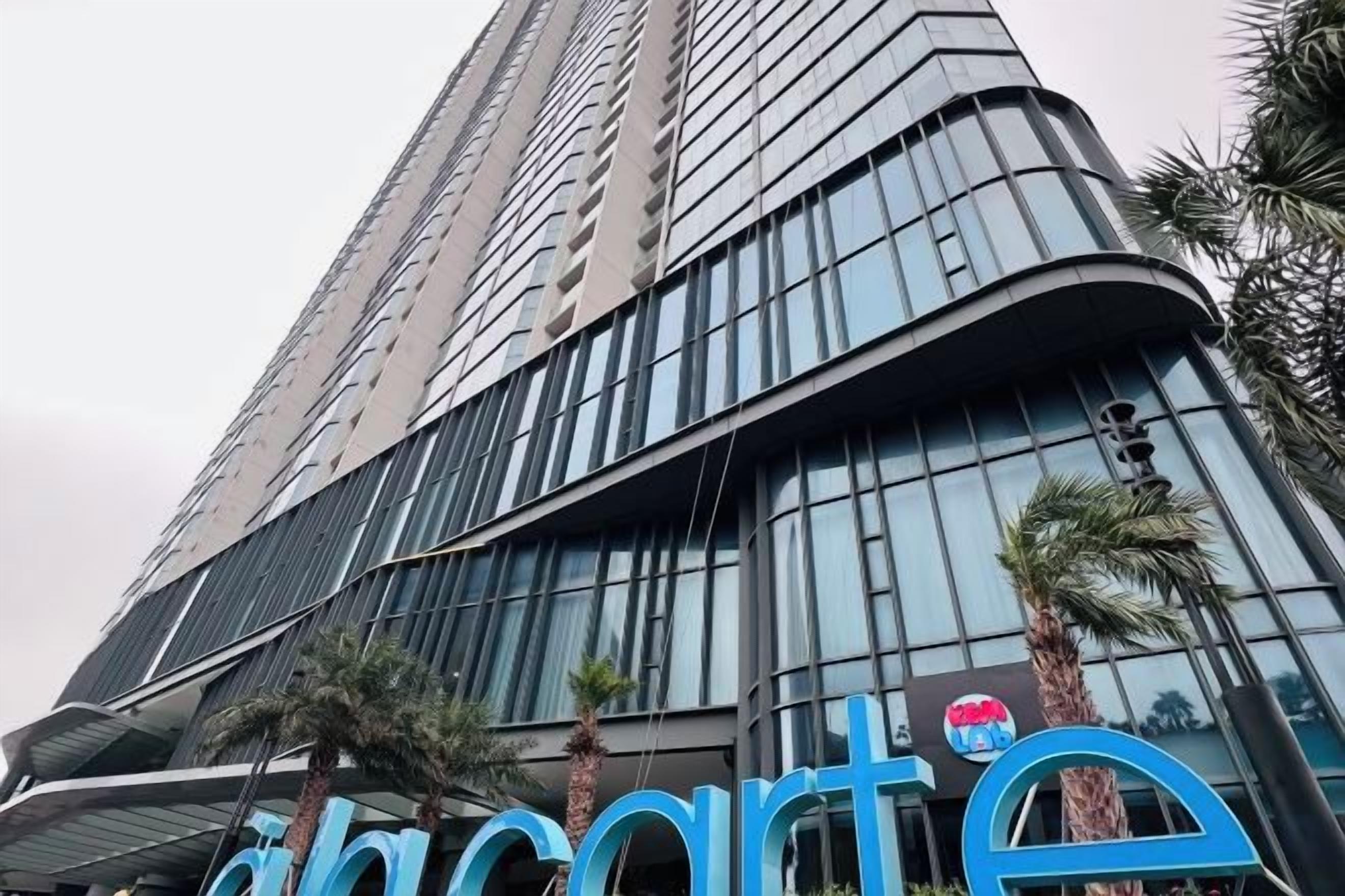 Un immeuble de grande hauteur à la façade incurvée, bordé de palmiers, et sur lequel on peut lire l’inscription « hôtel ».