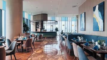 Un restaurant moderne doté d’un bar, de différents espaces pour s’asseoir et offrant une vue sur la ville.