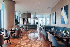 A modern restaurant with a bar area, seating arrangements, and a view of the city. - A La Carte Ha Long Bay Apartments by Kevin & Anna (Ha Long)