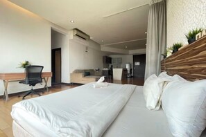 Habitación de hotel con una cama grande, un escritorio, una silla y una kitchenette al fondo.