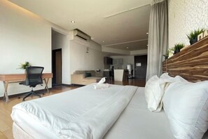 Habitación de hotel con una cama grande, un escritorio con silla, una kitchenette y una zona de estar con sofá.