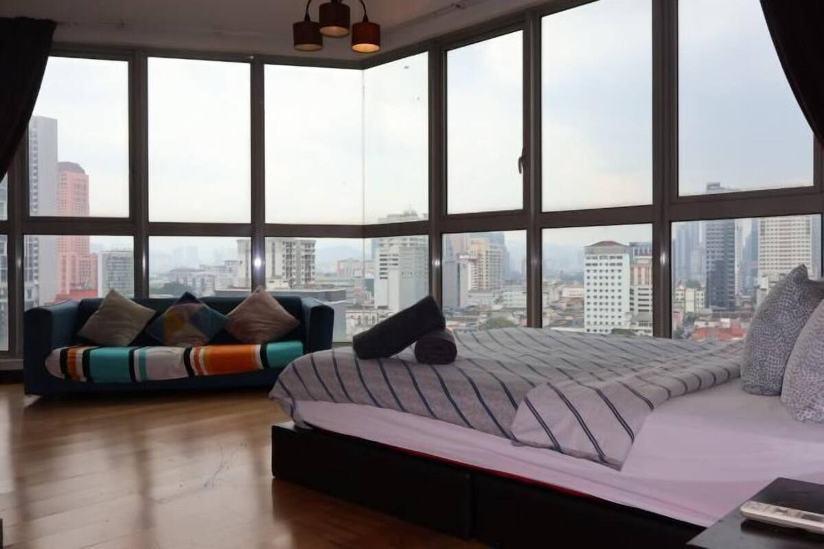 Une chambre située dans un immeuble de grande hauteur, dotée d’une grande fenêtre, d’un lit, d’un canapé et offrant une vue sur la ville.