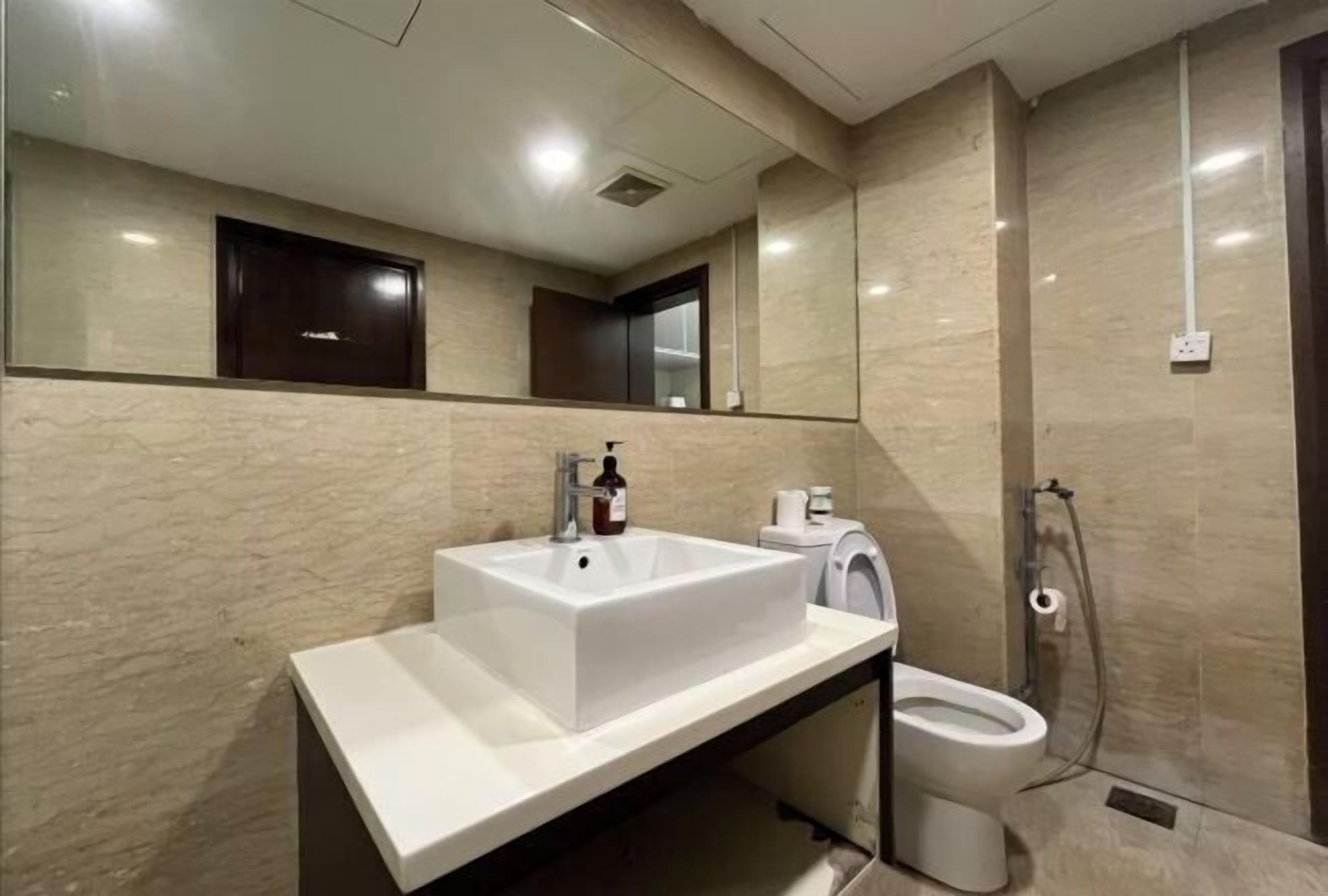A modern bathroom with a large mirror, a white sink, a toilet, and a shower area.
