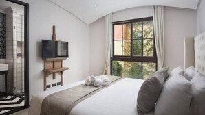 Ein modernes Hotelzimmer mit einem großen Bett, einem an einem Holzbalken befestigten Fernseher und Blick auf Bäume durch ein großes Fenster.