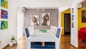 A dining area with a white table, blue cushioned bench, and two wall-mounted paintings.