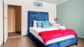 A bedroom with a large bed, a wooden door, a nightstand, and a painting on the wall.