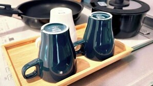 Un vassoio con due tazze blu scuro e un contenitore bianco su un tavolo di legno.