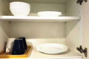 A kitchen with white cabinets, a white countertop, and a shelf with white bowls and plates. - Rakuyado Sanno (Osaka)