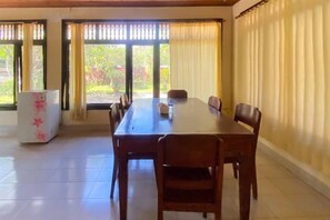 Un comedor con una mesa larga y sillas, un refrigerador y vistas a través de grandes ventanas.