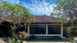 A building with a tiled roof, large windows, and a paved courtyard with potted plants. - Raja Asri Guest House Sanur Mitra RedDoorz (Bali)