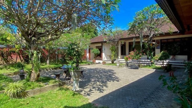 A courtyard with a paved walkway, surrounded by various potted plants and trees. - Raja Asri Guest House Sanur Mitra RedDoorz (Bali)