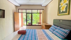 A bedroom with a bed, a nightstand, a window with a view of greenery, and a door. - Raja Asri Guest House Sanur Mitra RedDoorz (Bali)