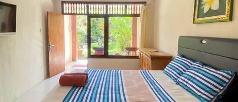 A bedroom with a bed, a nightstand, a window with a view of greenery, and a door.