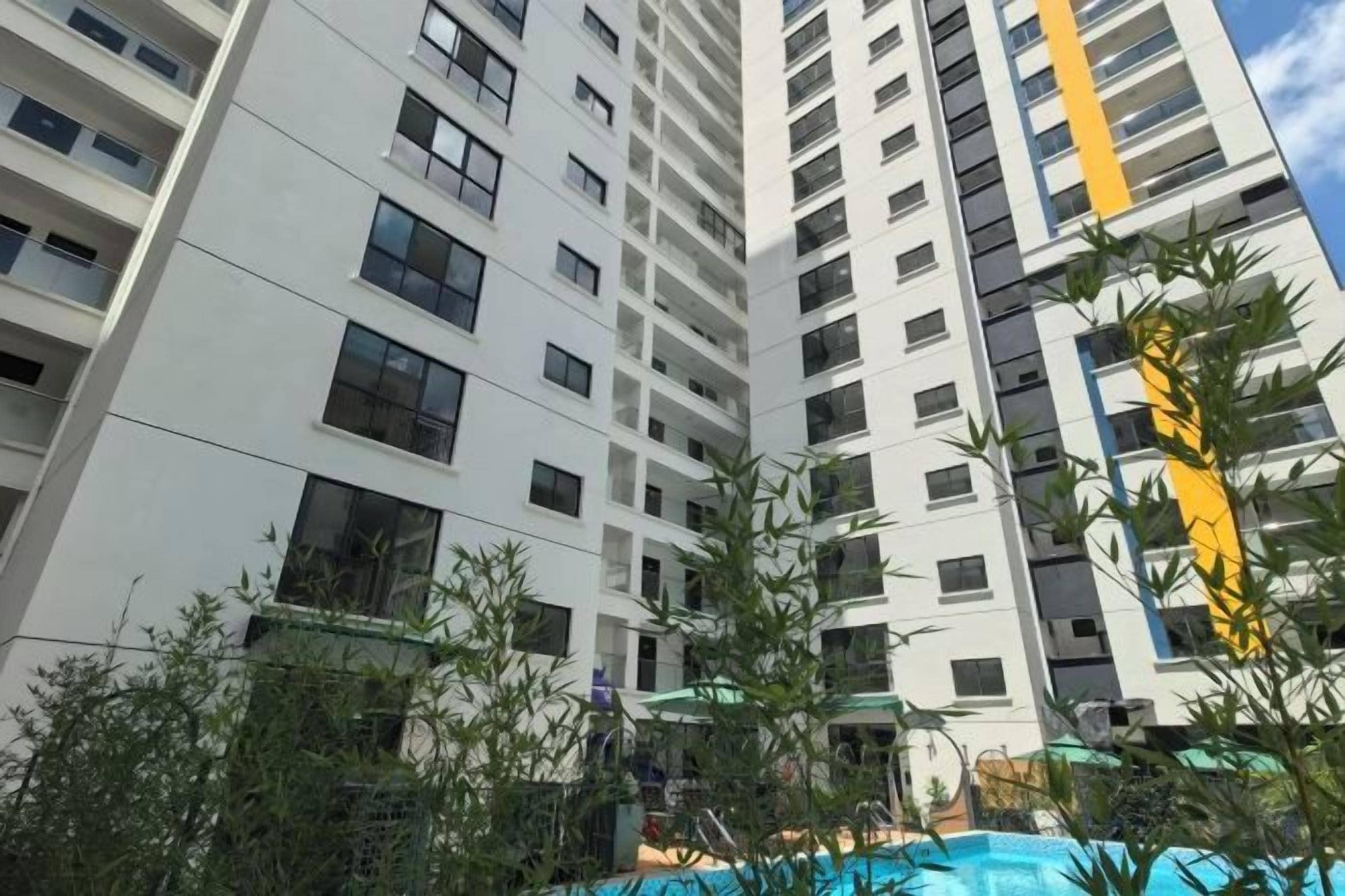 Een hoog appartementencomplex met meerdere balkons, een zwembad en omliggend groen.