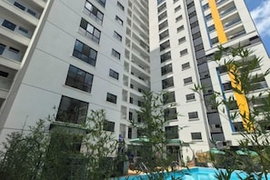 Een hoog appartementencomplex met meerdere balkons, een zwembad en omliggend groen.