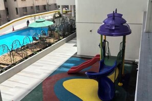 Zona de juegos infantiles con tobogán y estructura para escalar, junto a una piscina.