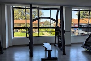 Een sportschool met een squatraam, bank en uitzicht op een woonwijk door grote ramen.