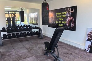 Un gimnasio con equipo de ejercicio, un saco de boxeo y un cartel motivacional en la pared.