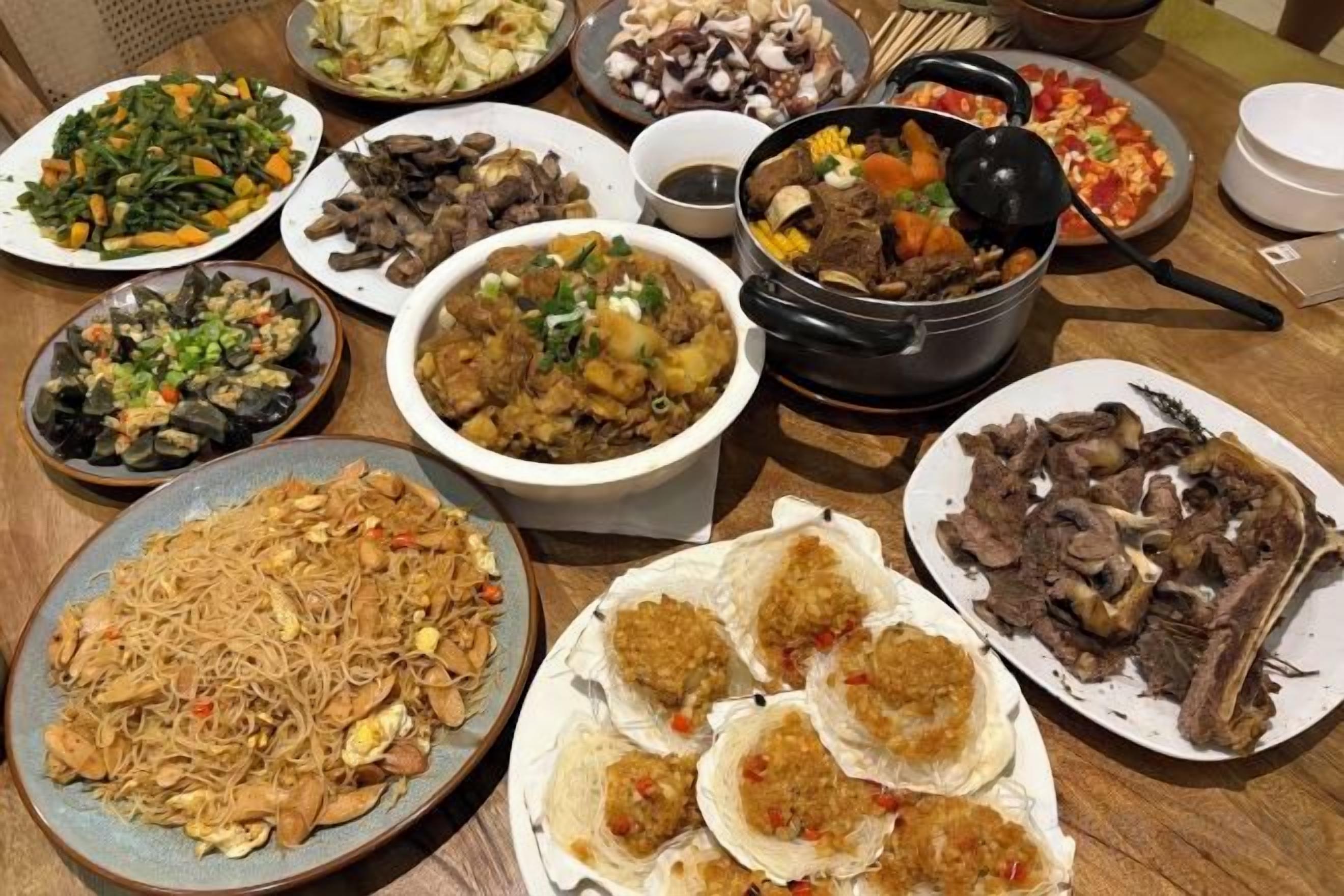 A variety of dishes on a table, including noodles, meat, and vegetables.
